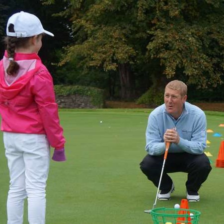 Coach providing golf instruction to young participant